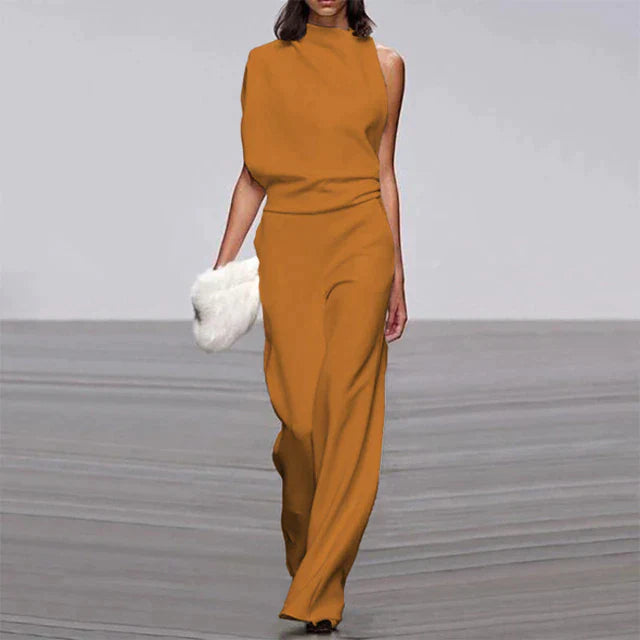 Frau in eleganter, ärmelloser, senffarbener Jumpsuit mit weitem Bein, hält weiße Clutch.