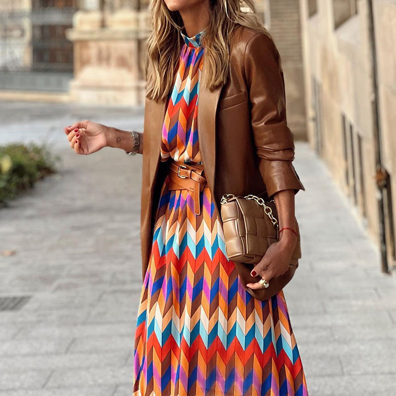 Frau in bunter Midi-Kleid mit geometrischem Muster und braunem Blazer auf Straße.