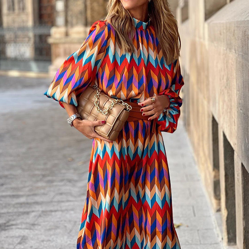 Frau in bunter Midi-Kleid mit geometrischem Muster, hält beige gesteppte Handtasche.