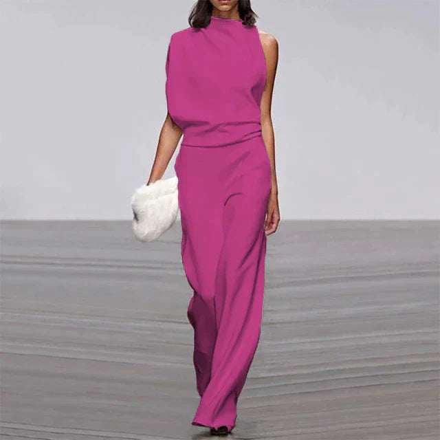 Frau in eleganter, ärmelloser, pinker Jumpsuit mit weitem Bein, hält weiße Clutch.